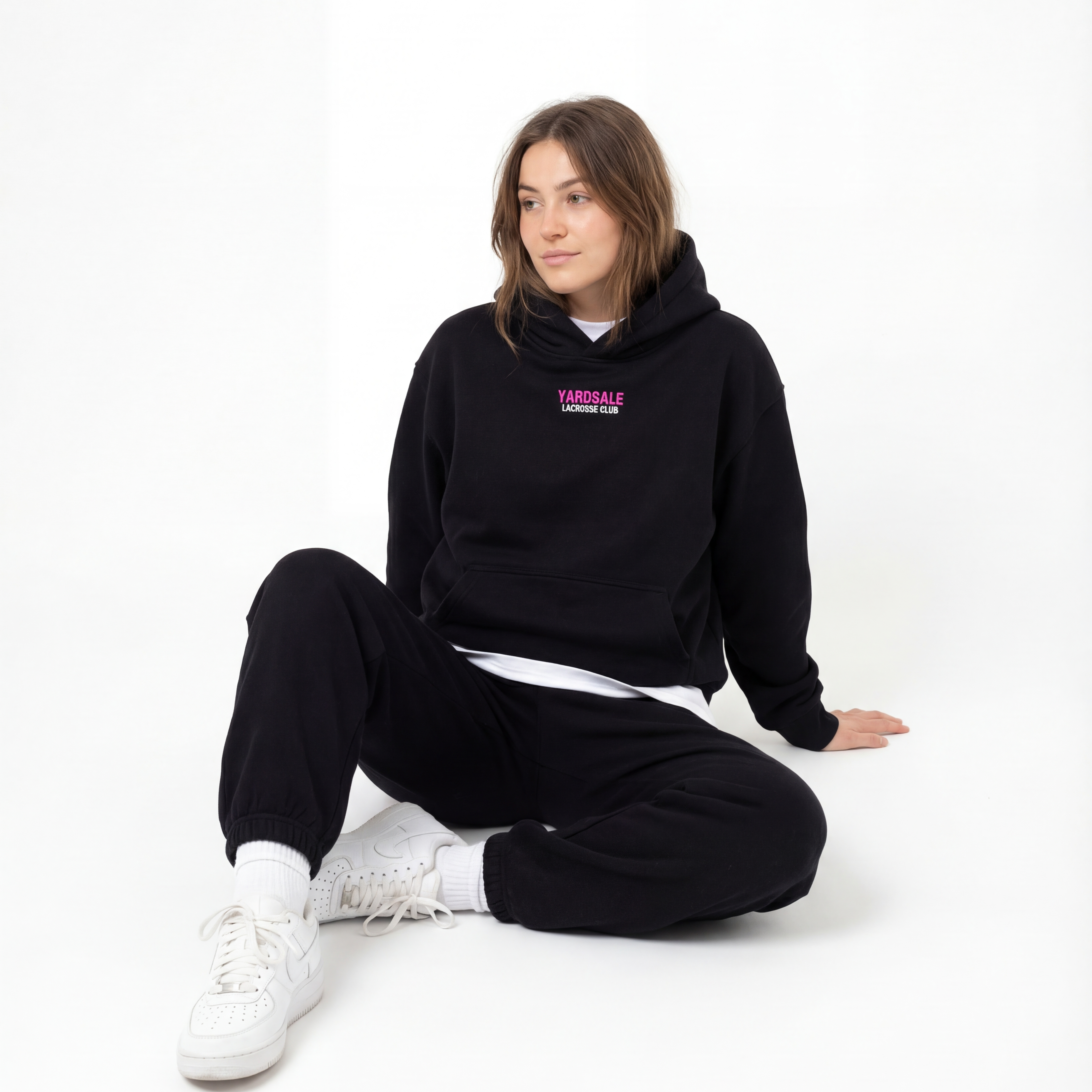 Person wearing a black hoodie with a logo sitting on a white background