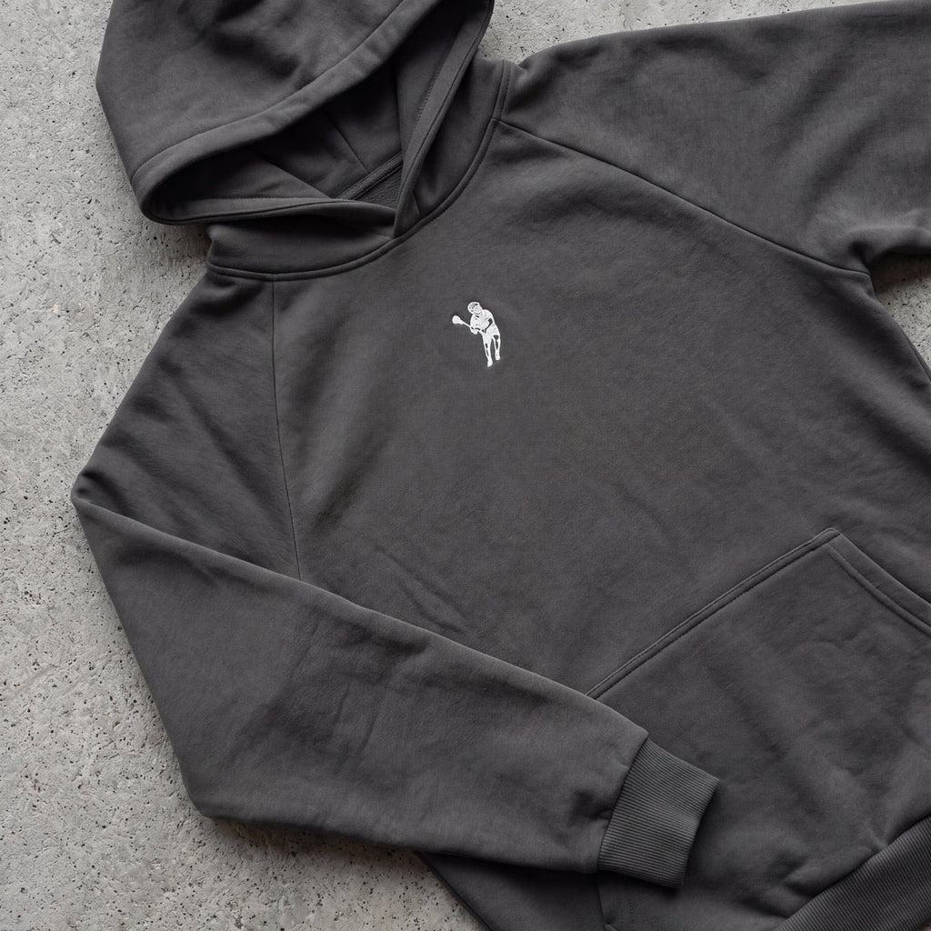 Dark gray hoodie with a small white logo on a concrete surface