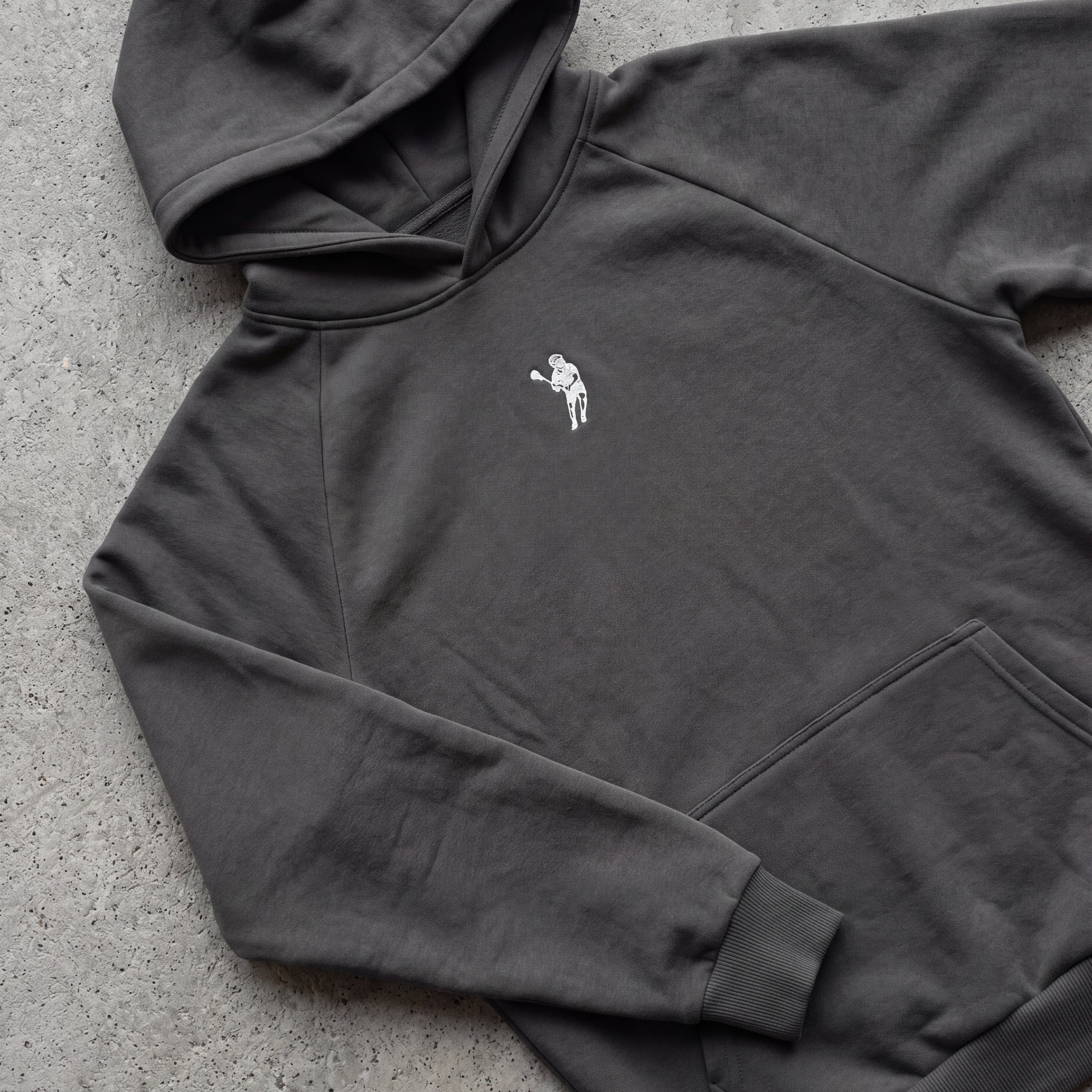 Dark gray hoodie with a small white logo on a concrete surface