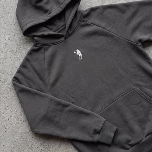 Dark gray hoodie with a small white logo on a concrete surface