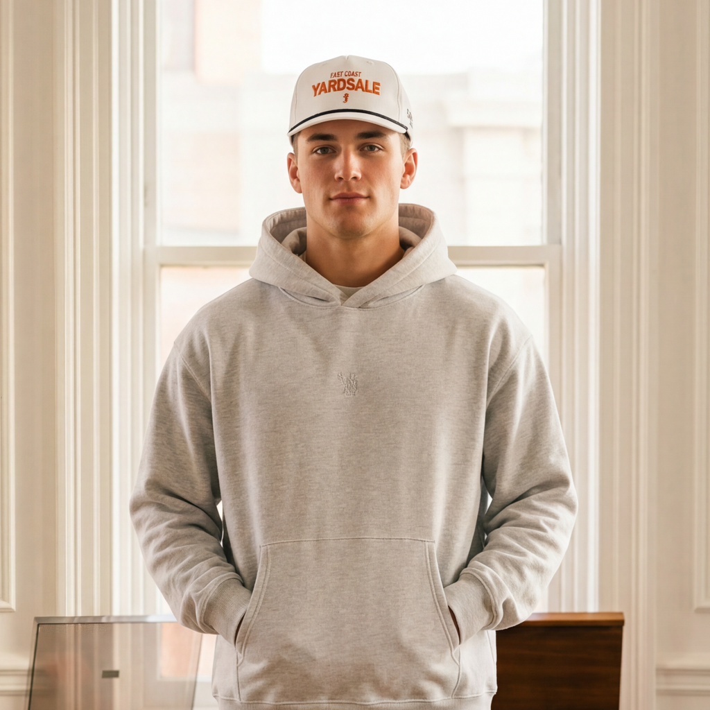 Person wearing a gray hoodie and blue jeans standing in a room with vintage furniture and suitcases.