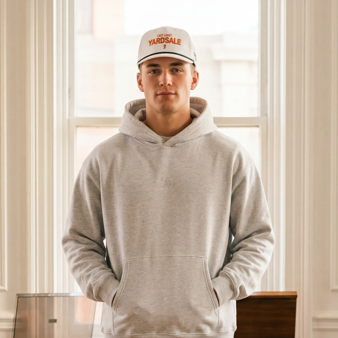 Person wearing a gray hoodie and blue jeans standing in a room with vintage furniture and suitcases.