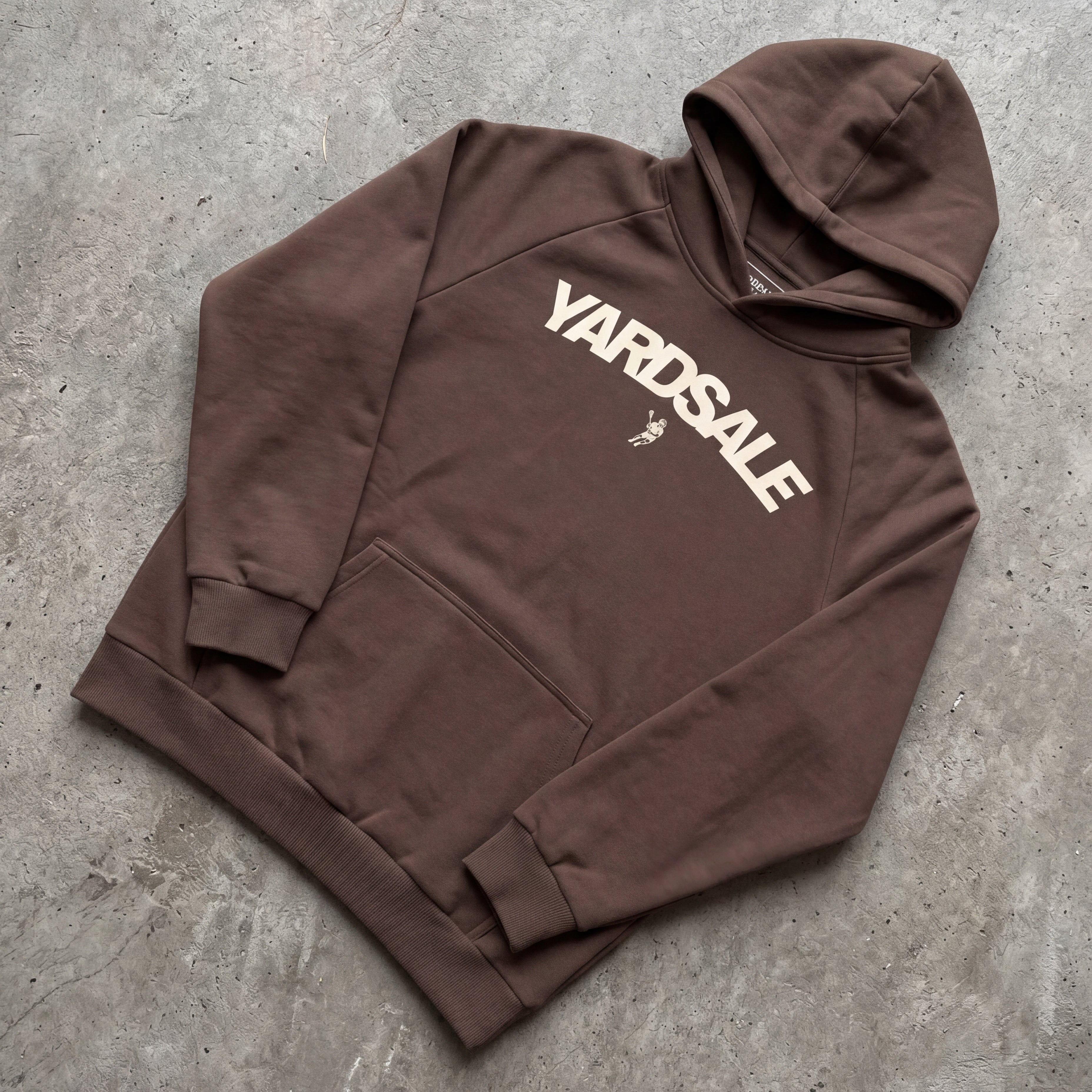 Brown hoodie with 'Yardsale' logo on a gray concrete surface