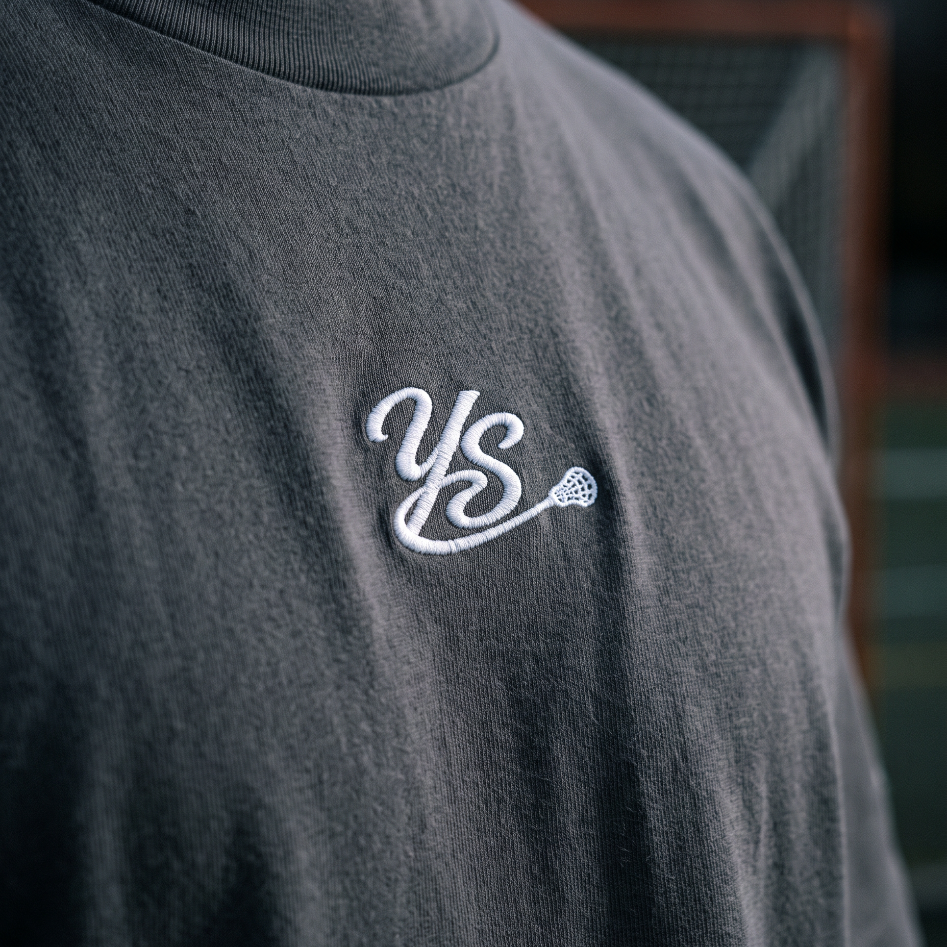 A close-up of a person wearing a dark charcoal gray t-shirt with a white embroidered 'YS' logo on the chest, set against a blurred background.