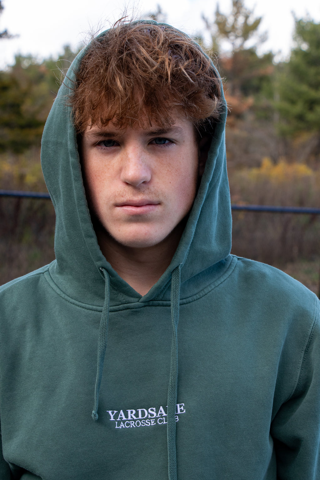 Person wearing a green hoodie with 'Yardsale Lacrosse Club' text outdoors.