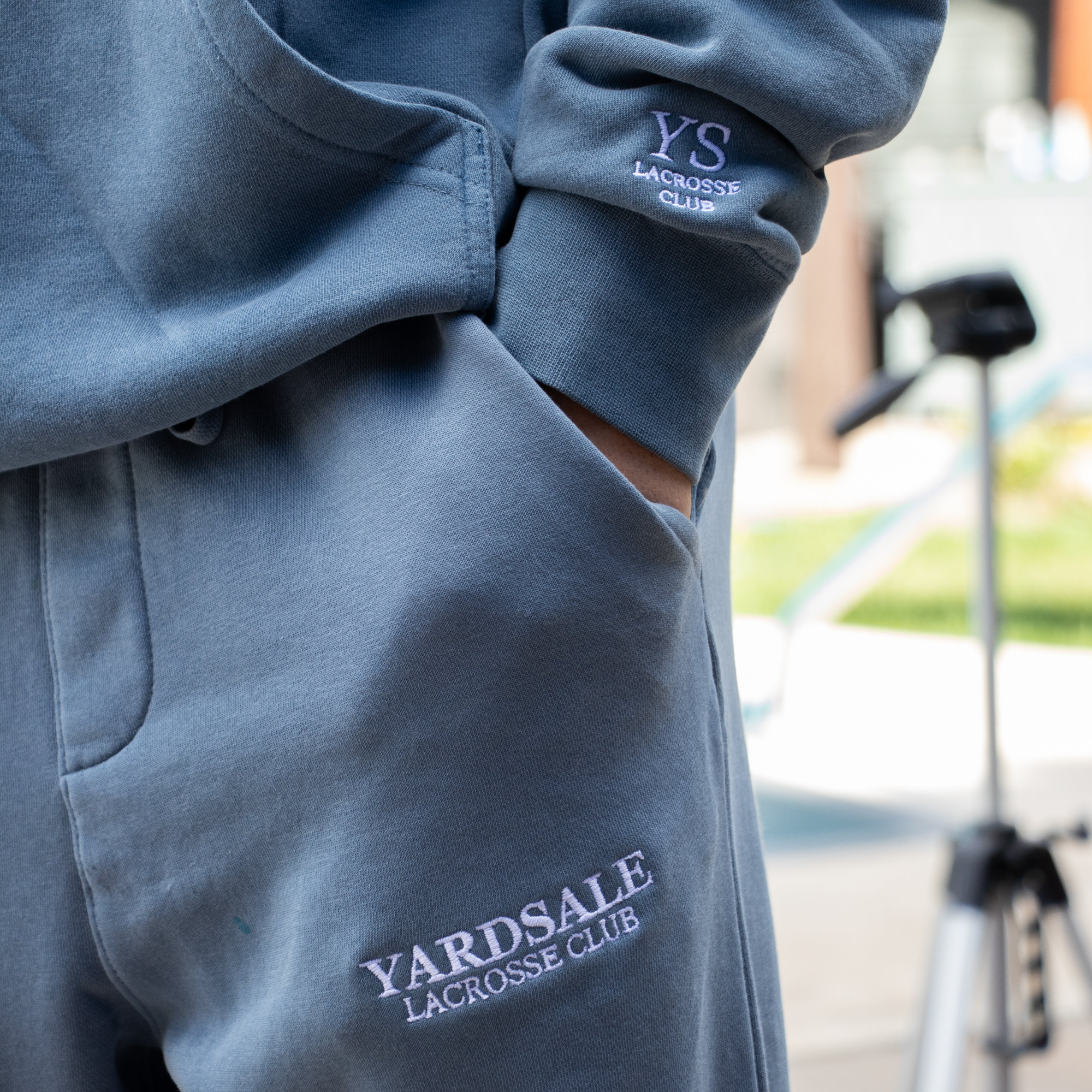 Blue tracksuit with 'Yardsale Lacrosse Club' branding on a blurred outdoor background