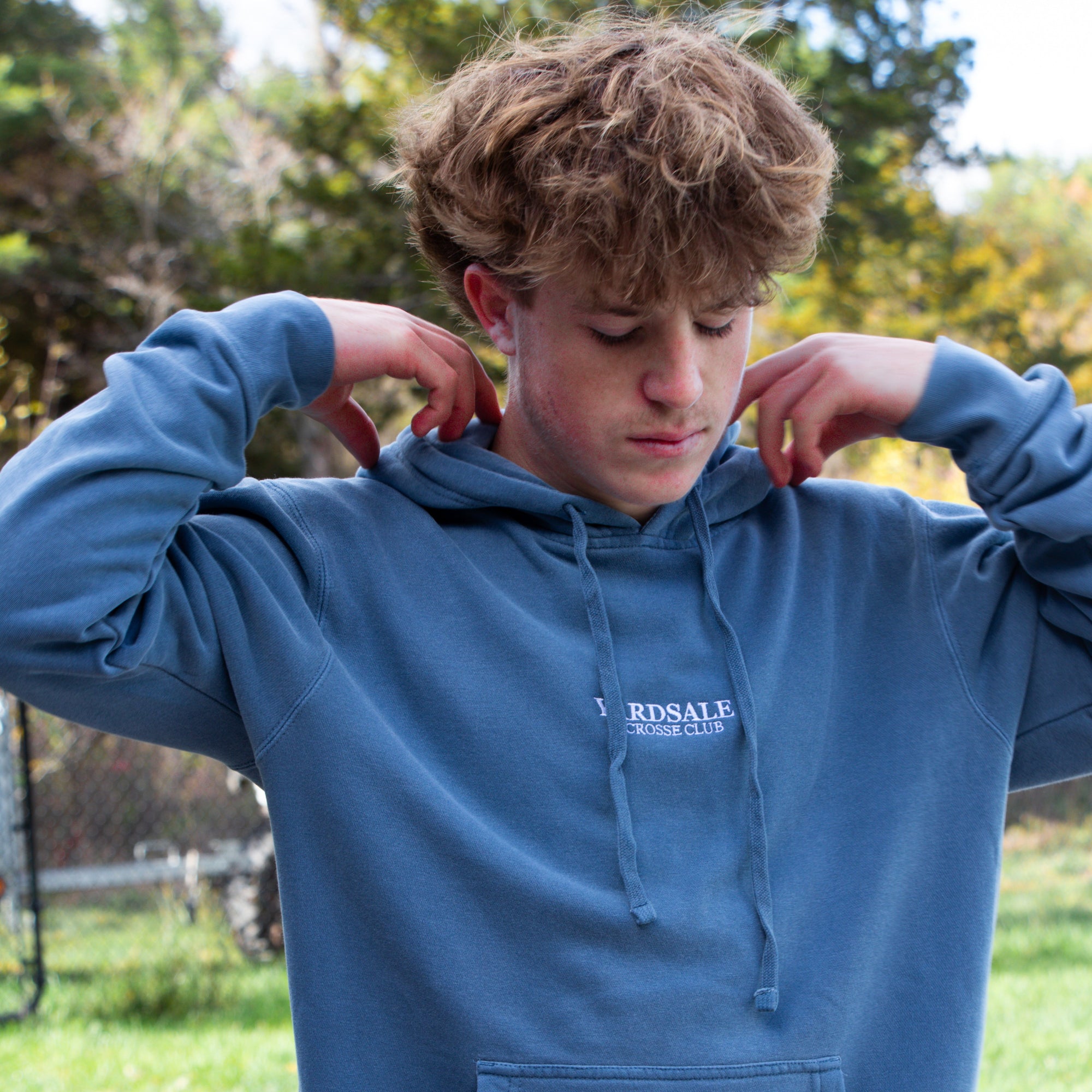 Person wearing a blue hoodie with a visible brand logo outdoors.