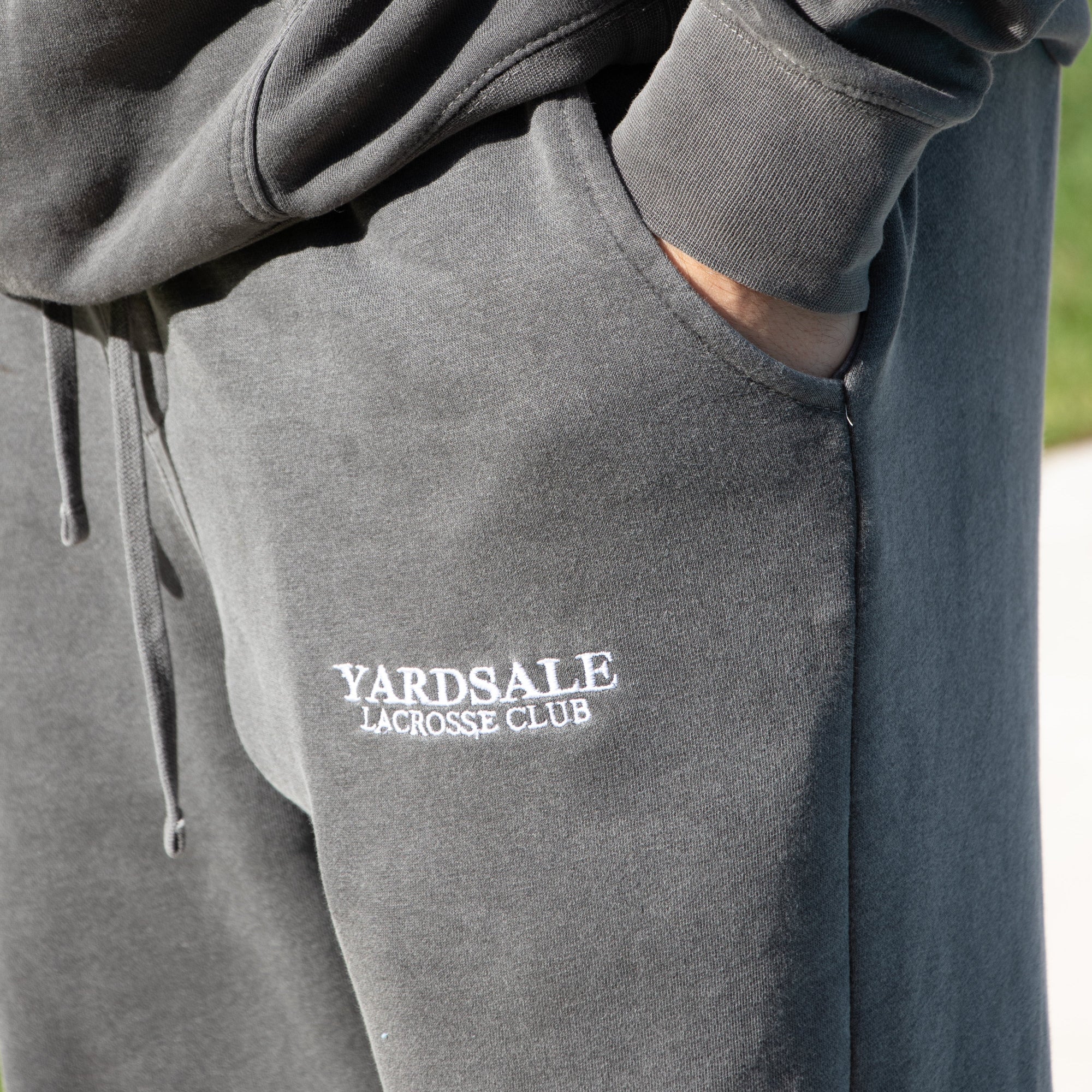 Gray sweatpants with 'Yardsale Lacrosse Club' logo on a blurred background