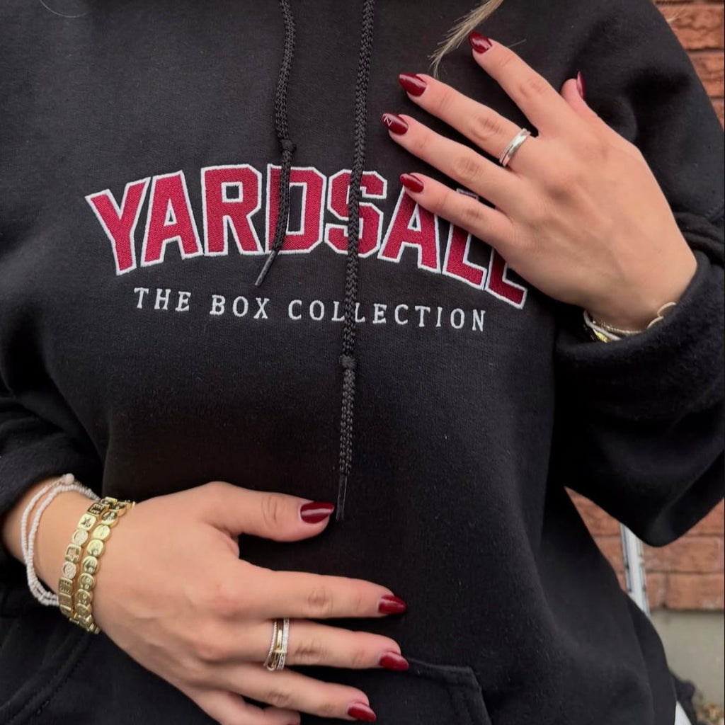 Person wearing a black hoodie with 'Yardsale' branding, standing against a brick wall.