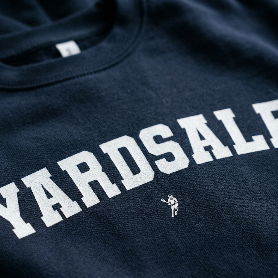 Close-up of a navy blue crewneck sweatshirt featuring the word 'YARDS' in large white varsity-style block letters, with a small white football player graphic underneath.