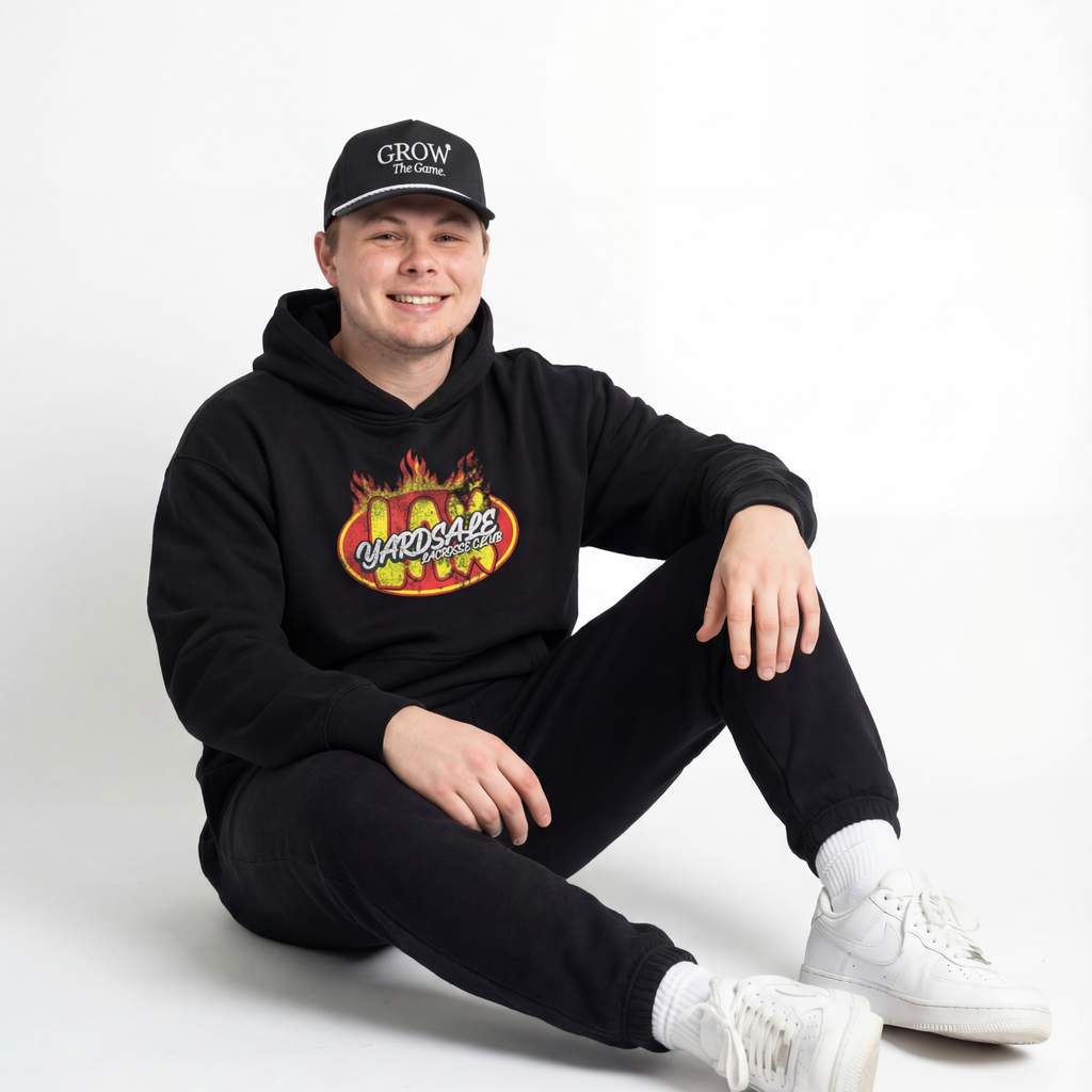 Person wearing a black hoodie with a colorful graphic and text, sitting on a white background