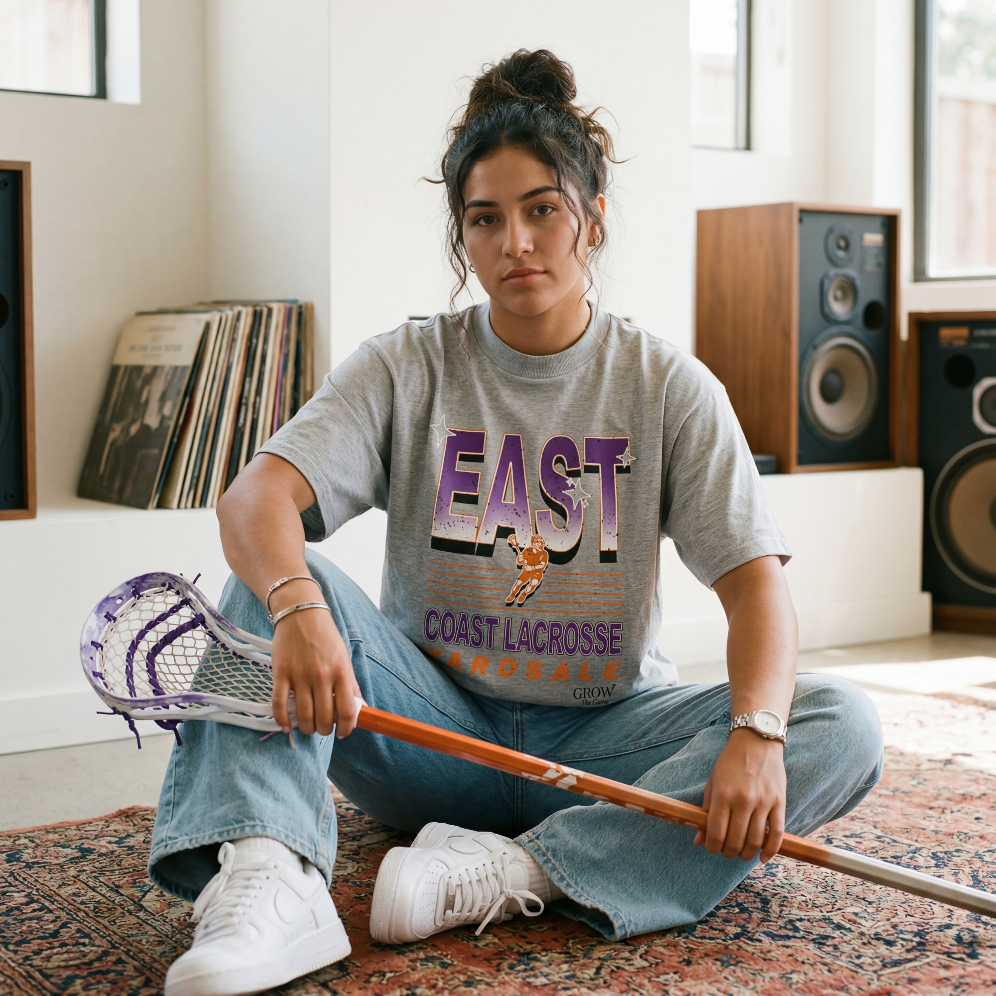 Person sitting on a rug holding a lacrosse stick in a room with speakers and records.
