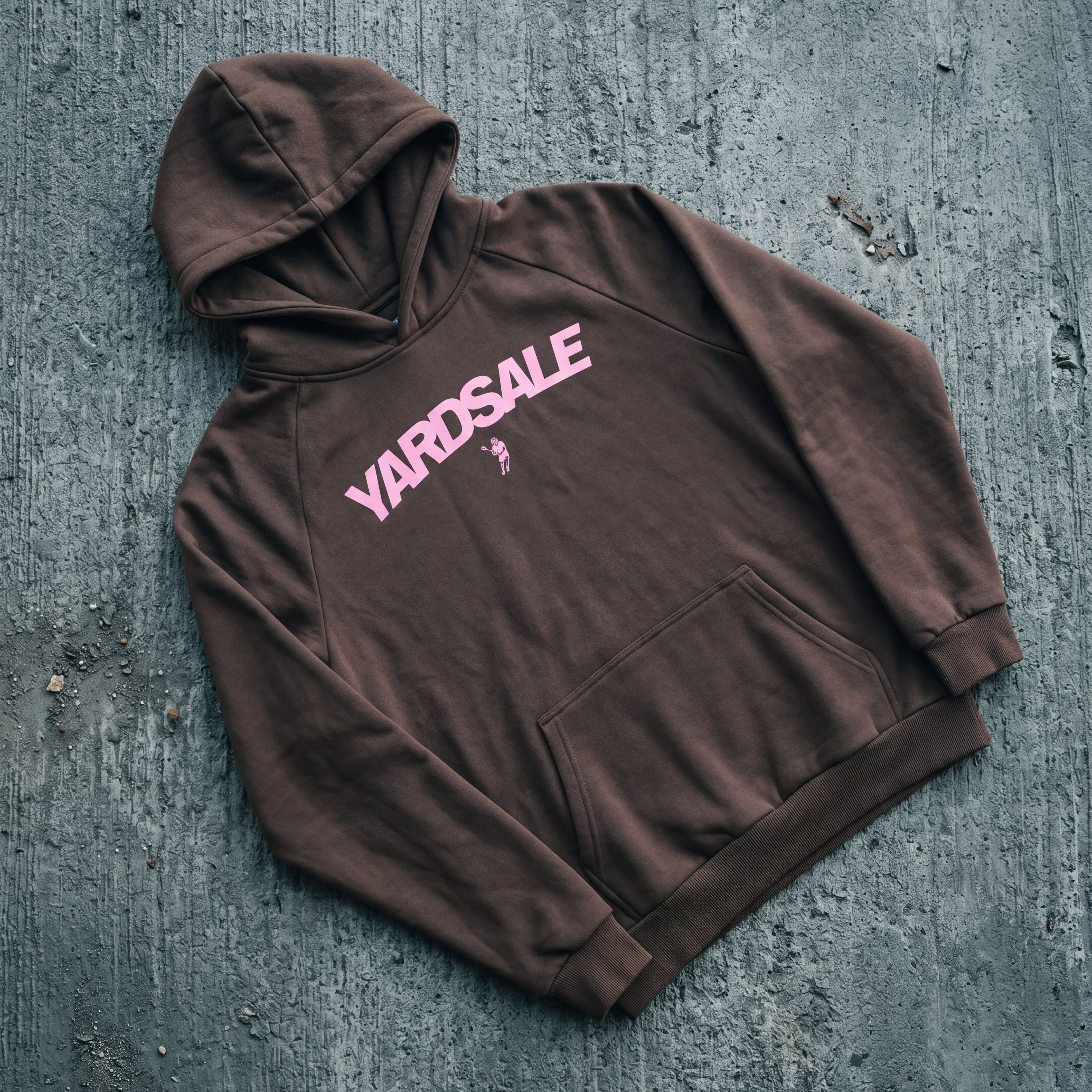 Brown hoodie with 'Yardsale' text on a textured gray surface