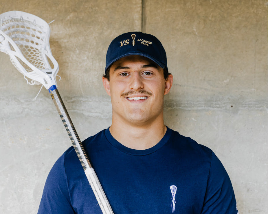 Man holding a lacrosse stick against a concrete wall
